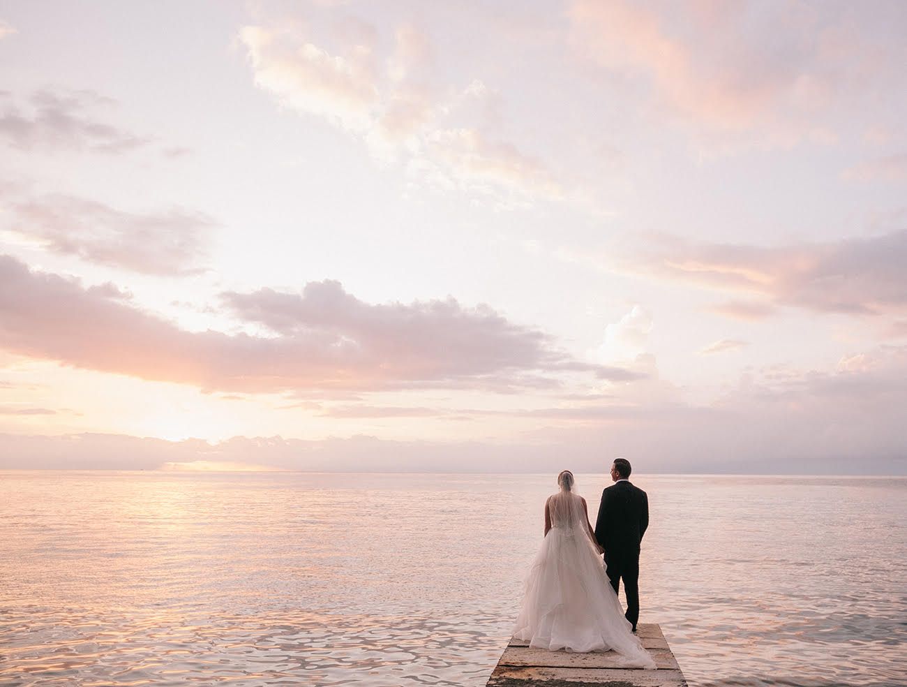 Bride and groom on pier staring sun setting over the water