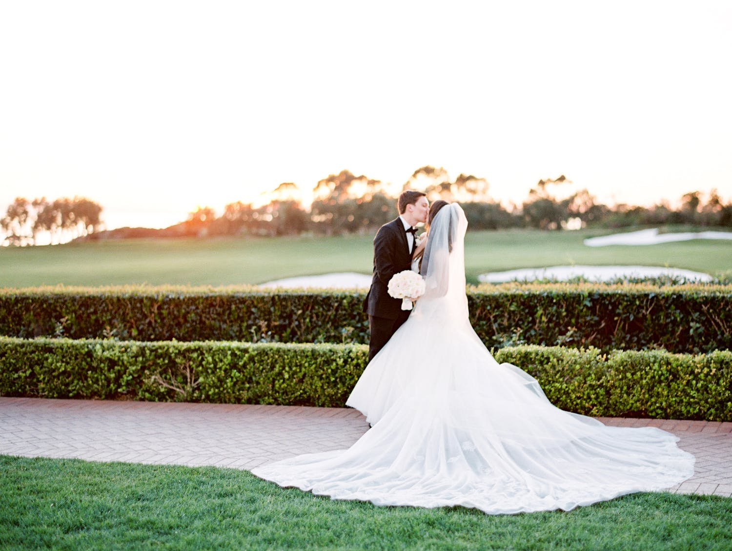 bride and groom kiss in front of gold course