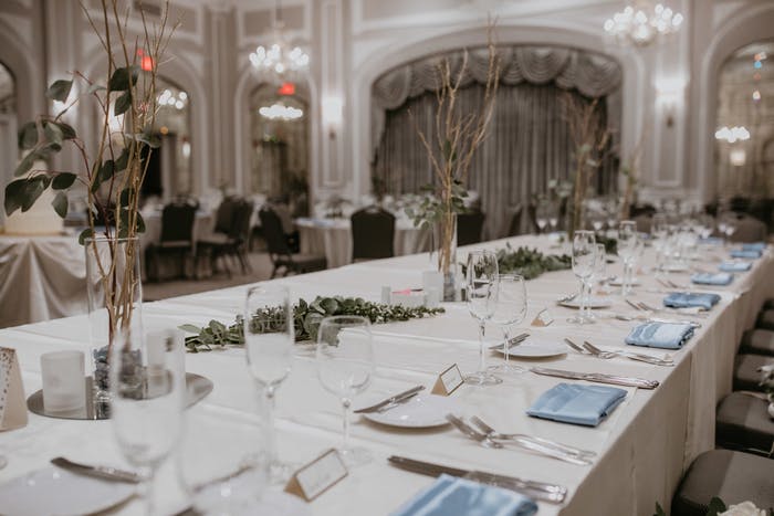 a long table extends through the room with a white tablecloth decorated with elegant place settings and branches and greens.