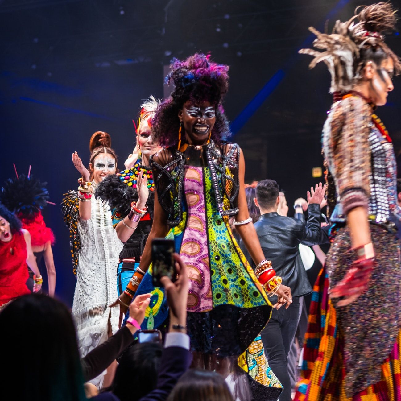 Models walk down the runway with big smiles on their faces, audience members snap pictures and clap.