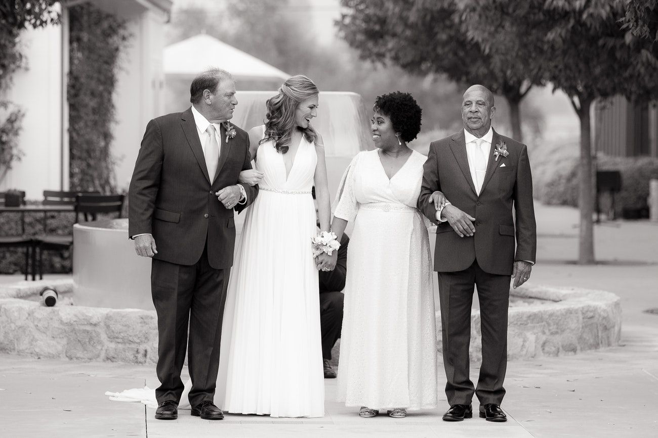 2 brides stand in the middle of each of their fathers, preparing to walk down the aisle.
