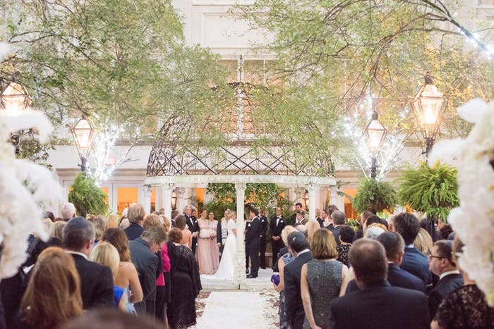 a metal gazebo above a bride and groom saying vows while family and friends watch