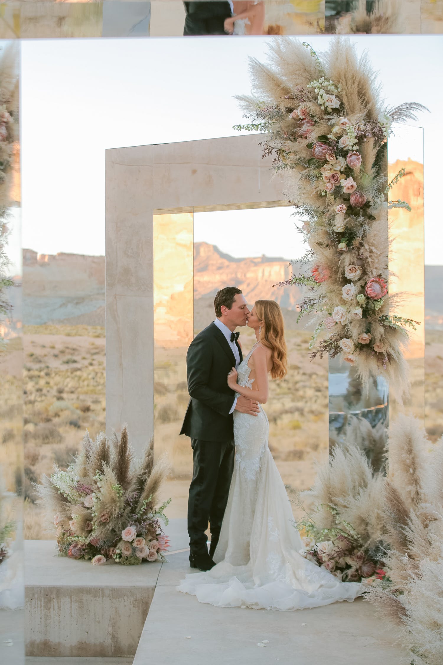 bride and groom kiss under rectangular, mirrored archway with desert backdrop