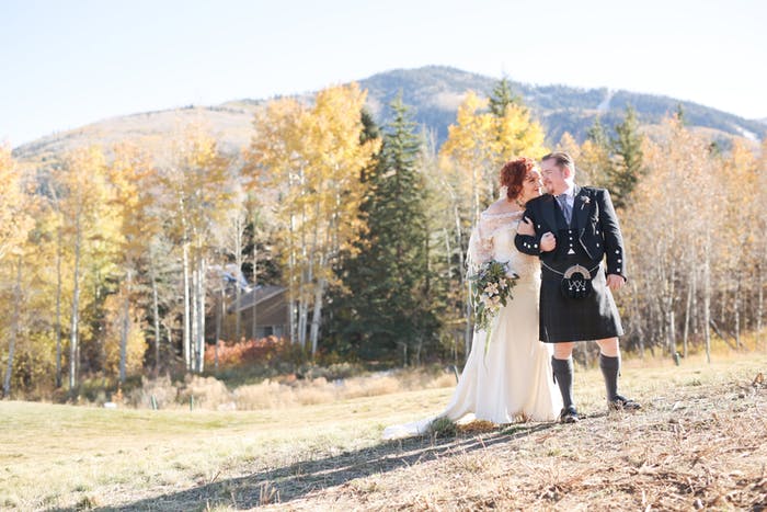 Bride and groom in field with forest and mountain in the background