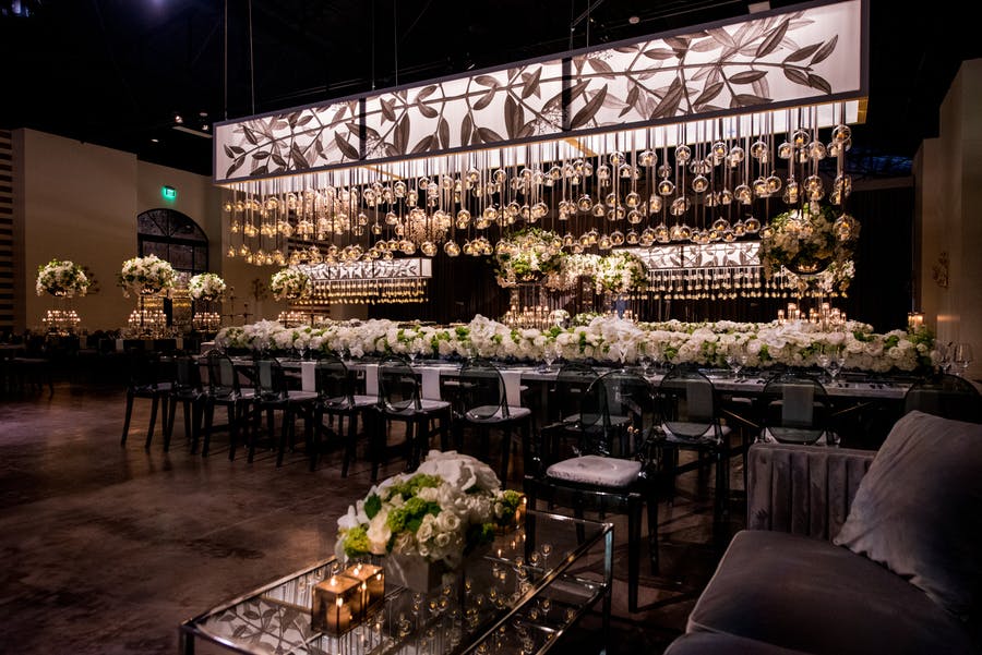 Bar with white flowers and glasses hanging across from candles making them appear to glow.
