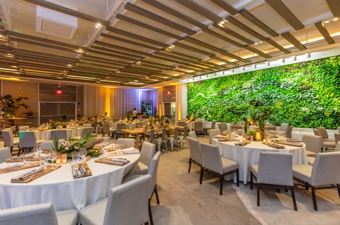 Wooden slats as the ceiling with greenery on a wall. Tabes with white linens