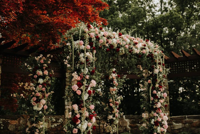 An archway covered in pale pink and white florals mixed with draping greenery