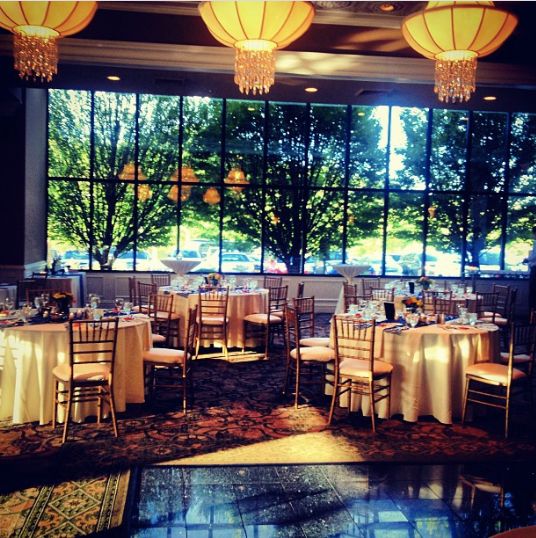 Concorde Banquets baby shower venue in Chicago with tables with white linens and wooden chairs. Large paned windows look out to greenery and trees