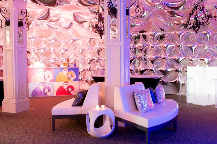 50th Birthday Party With Reflective Wall as a Backdrop with Modern White Couches Back to Back and Pink and Purple Lighting | PartySlate