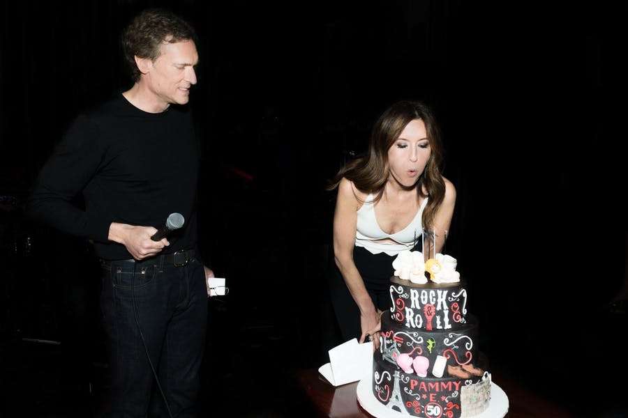 A Women Blows Out the Candles to Her 50th Birthday Cake and a Man Stands Beside Her with a Microphone | PartySlate