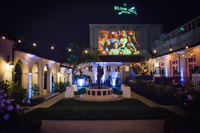 A big outdoor space with a screen high up and blue uplighting close to the stage