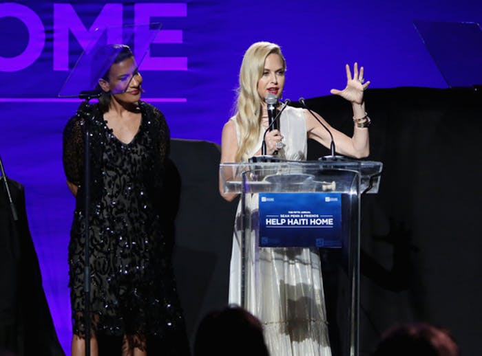 two women stand at a podium with a screen behind them.