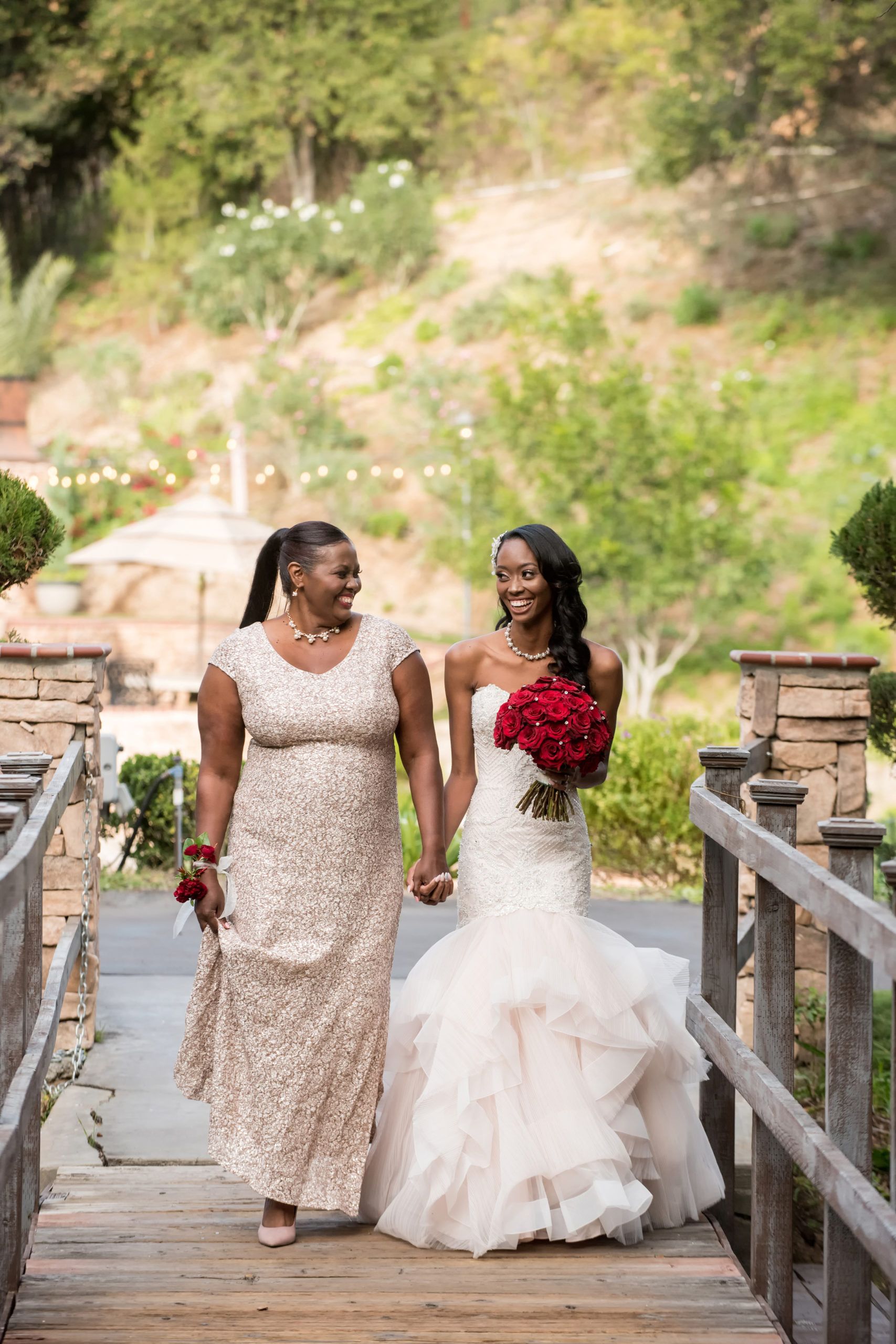 Mother walks bride holding a red-rose bouquet down the aisle.
