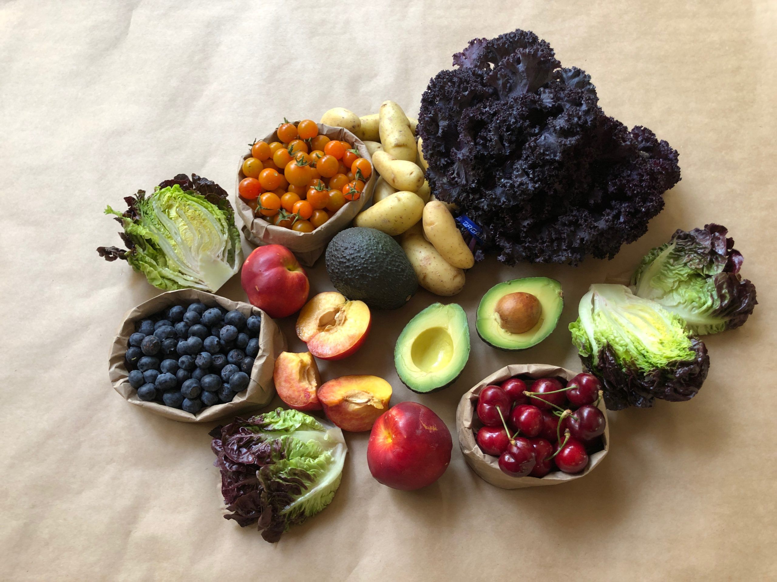 Fresh fruit and veggies on a taupe tablecloth.