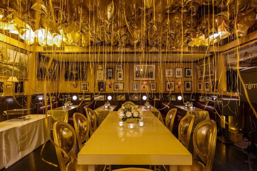 looking down the length of a long table. A wash of yellow/orange light and balloons with long ribbons hanging down
