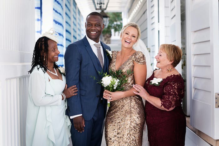 A bride and groom take a picture with their mom on each side in a quiet outdoor corridor.