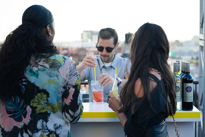 A bartender in the center placing straws in a drink while two women stand on either side of him