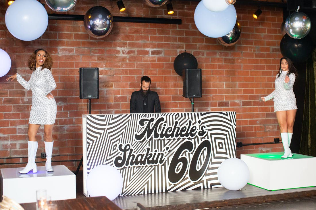 A DJ stand with a 60s theme and two 60s dancers on either side on a raised platform