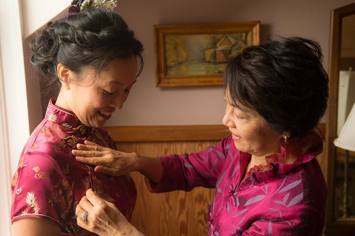 A Mother, wearing a hot pink Cheongsam, smooths out her daughter's hot pink Cheongsam