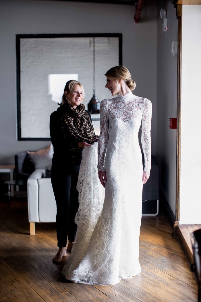 A brie standing in the foreground in her dress with her mother in the background helping her train