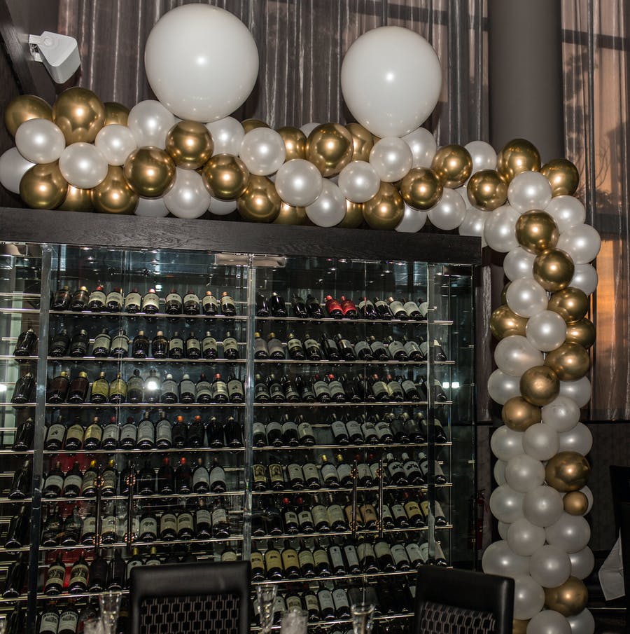 A full wine fridge with white and gold balloons on the border