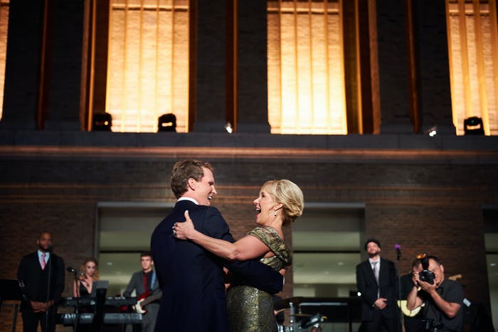 A mother dances with her son on the dance floor. three large windows are behind them