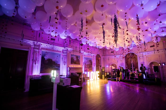 A large balroom dance floor lit up purple with white balloons covering the cieling