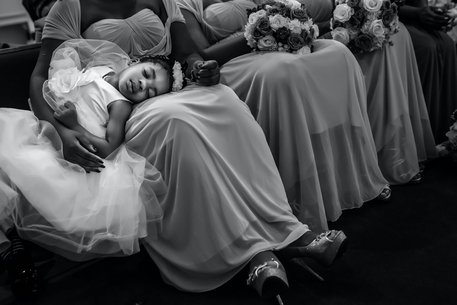 Child in white dress falls asleep on mother's lap.