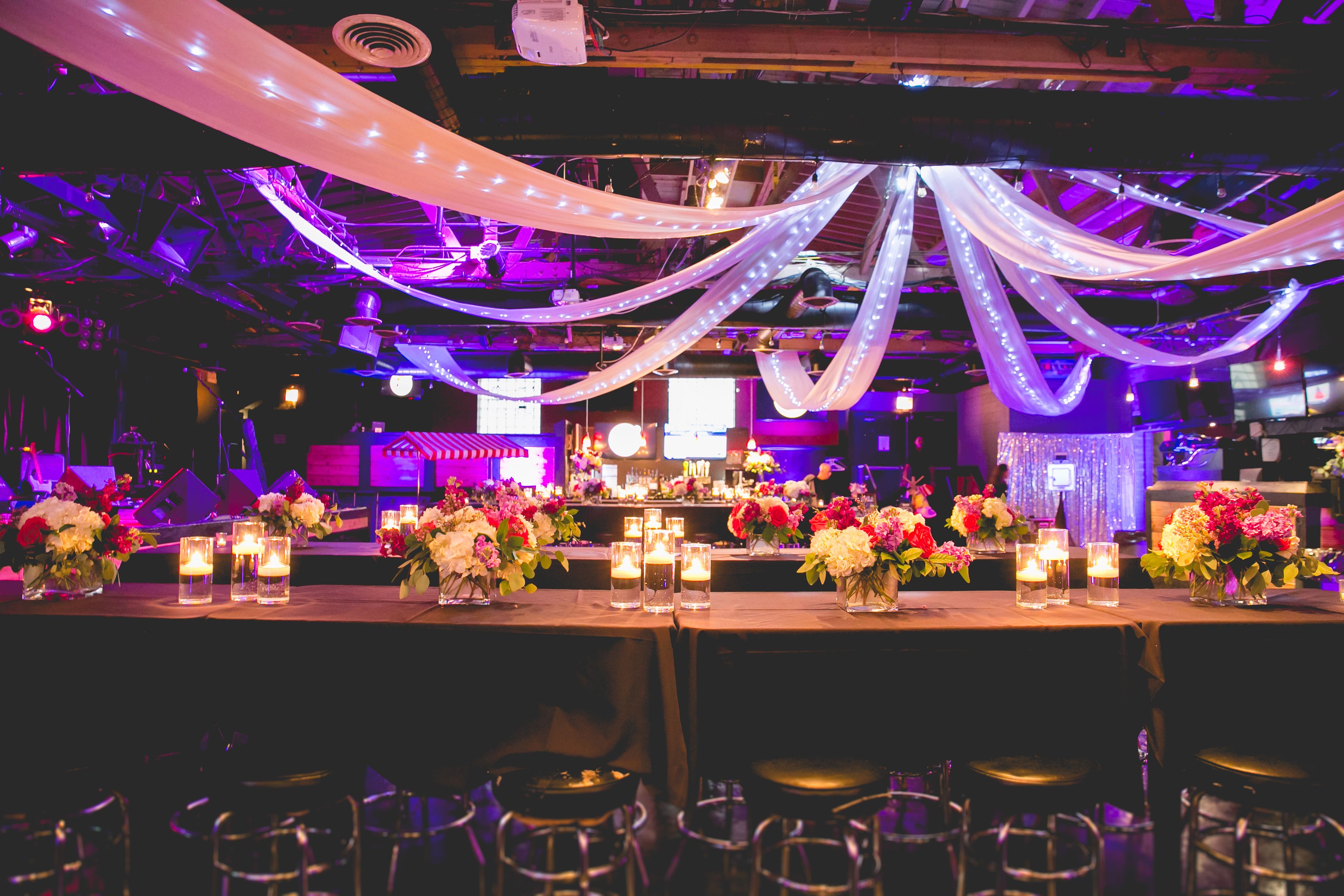 Festive wedding reception with long tables and lite up linen hanging from the ceiling | PartySlate