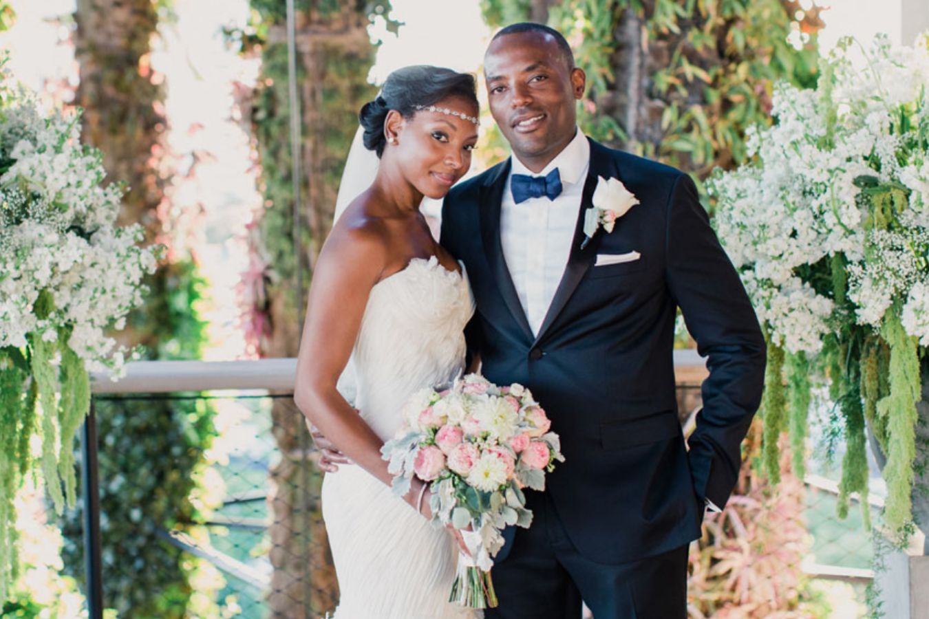 Bride and Groom Pose Before Lush Backdrop of Greenery | PartySlate