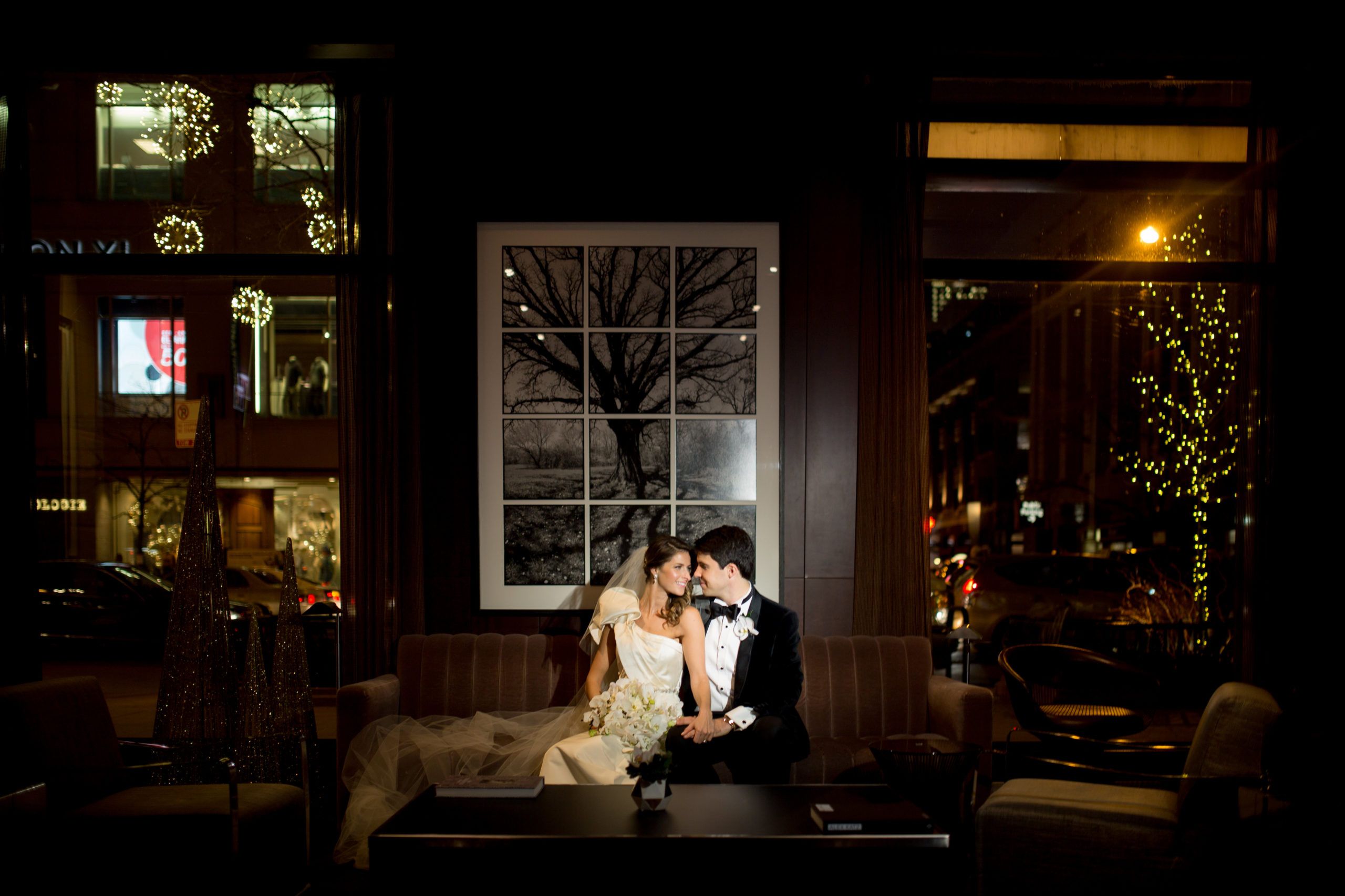 Bride and Groom Sit on Sofa at Park Hyatt Chicago In Dim Room With Wood Paneled Walls | PartySlate