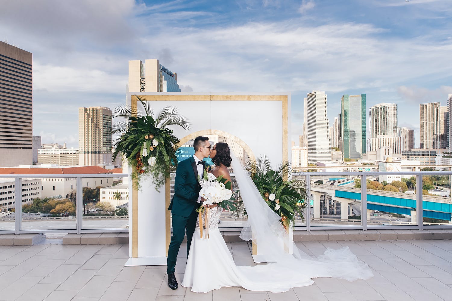 Bride and Groom Kiss In front of Modern Arch at PENTHOUSE at Riverside Wharf Overlooking Skyline | PartySlate