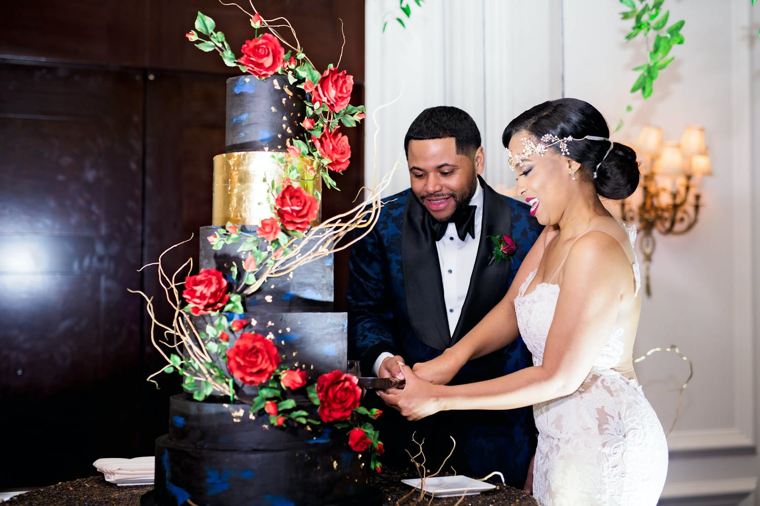 Bride and Groom Cut Into Glamorous Rose-Decorated Black and Gold Cake at Wedding Planned by The Savvy Consultants of Houston, TX | PartySlate