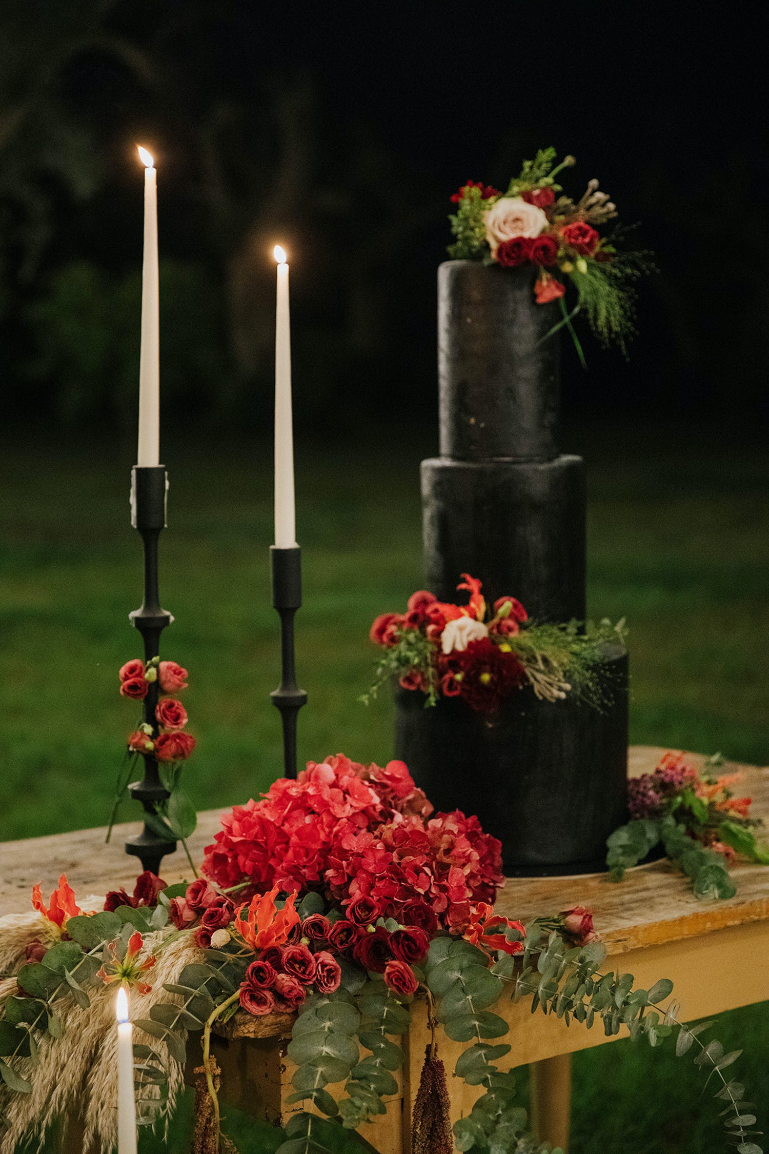 Three tier skinny black wedding cake with two red flowers | PartySlate