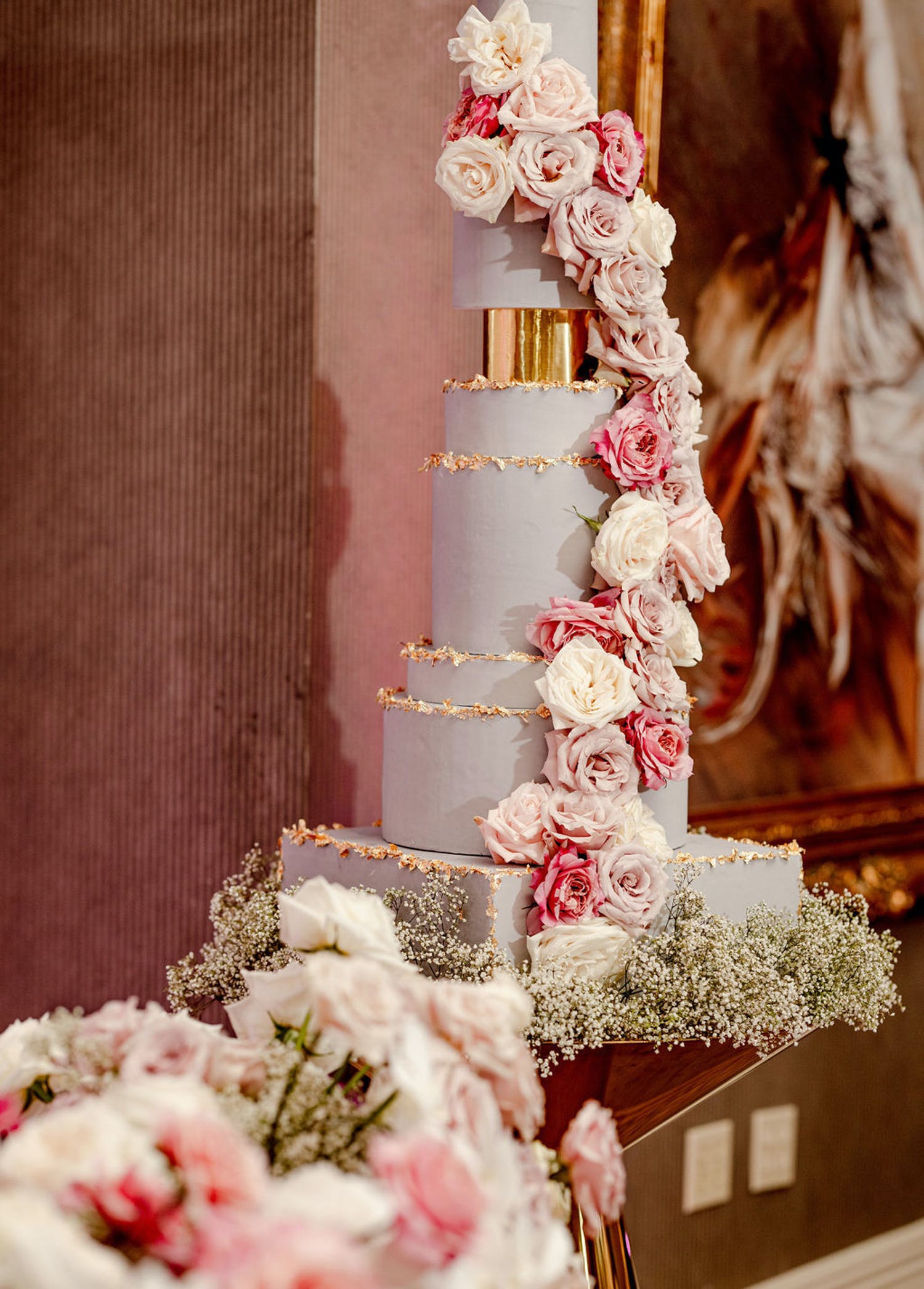 Towering White and Gold Wedding Cake With Cascade of Pink Roses and Bed of Baby's Breath Designed by Déjà vu Sweets | PartySlate