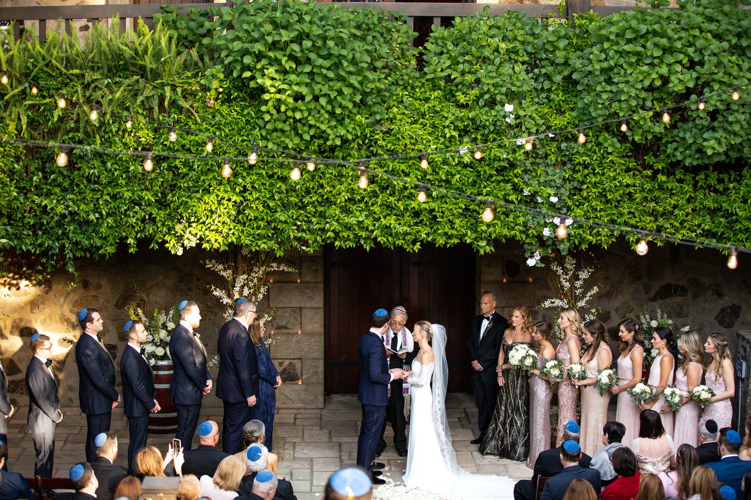 Bride and groom under a vibrant green wall altar at V Sattui Winery, a Napa winery estate | PartySlate