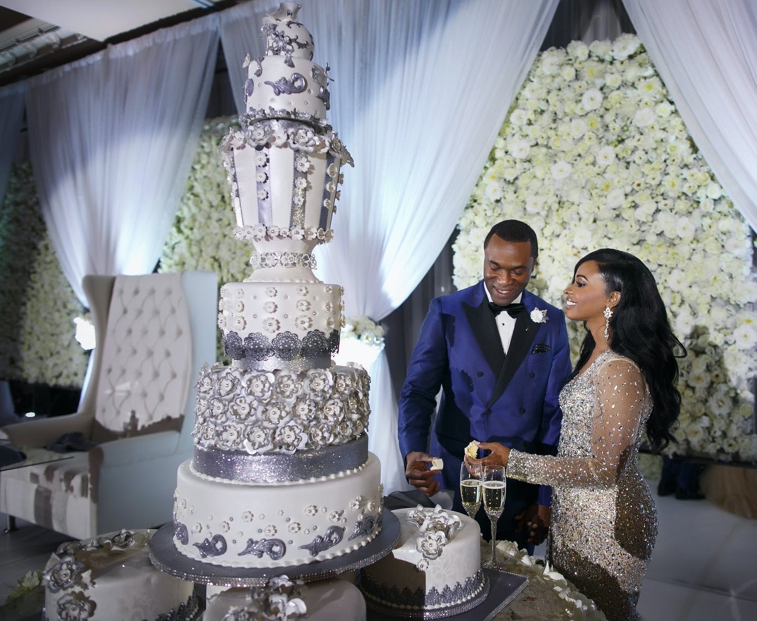 Bride and groom cut into towering white and silver luxury wedding cake designed by Edet Okon of Houston, TX | PartySlate