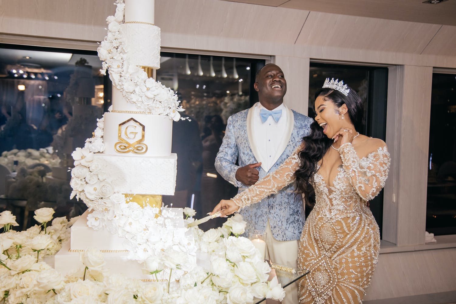 Tall white wedding cake of circle and square tiers with with gold monogram symbol | PartySlate