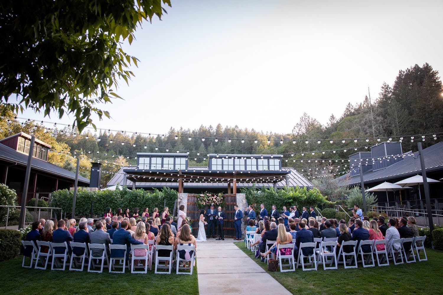 Outdoor ceremony with a barrel altar and dangling lights at Brasswood Estate in Napa, CA | PartySlate