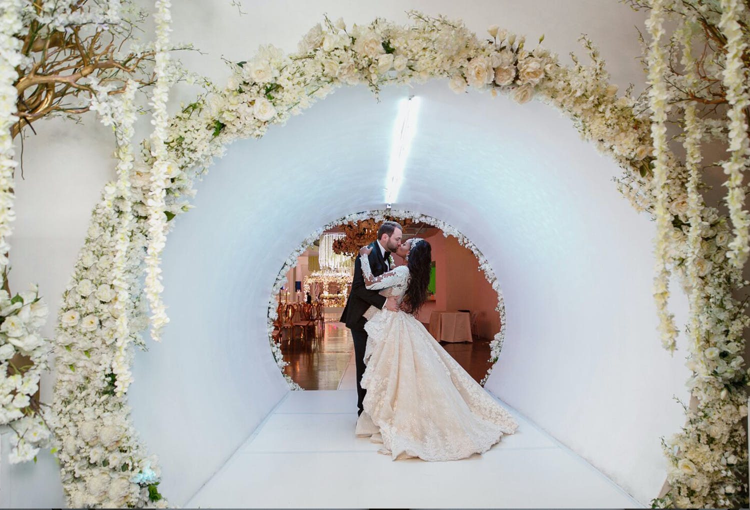 Bride and Groom Kiss in White Tunnel Entrance Decorated with White Flowers at Wedding Planned by Dure Events of Houston, TX | PartySlate