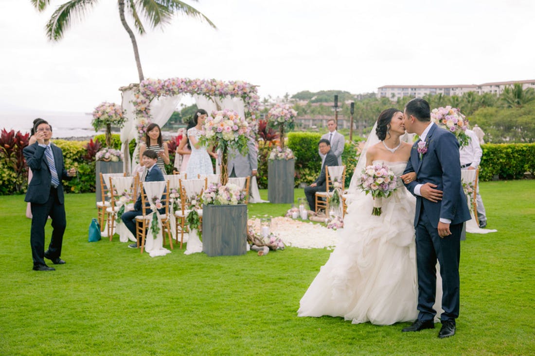 Couple Kissing As they walk Away From The Alter With The Ocean an other Guests Behind Them | PartySlate