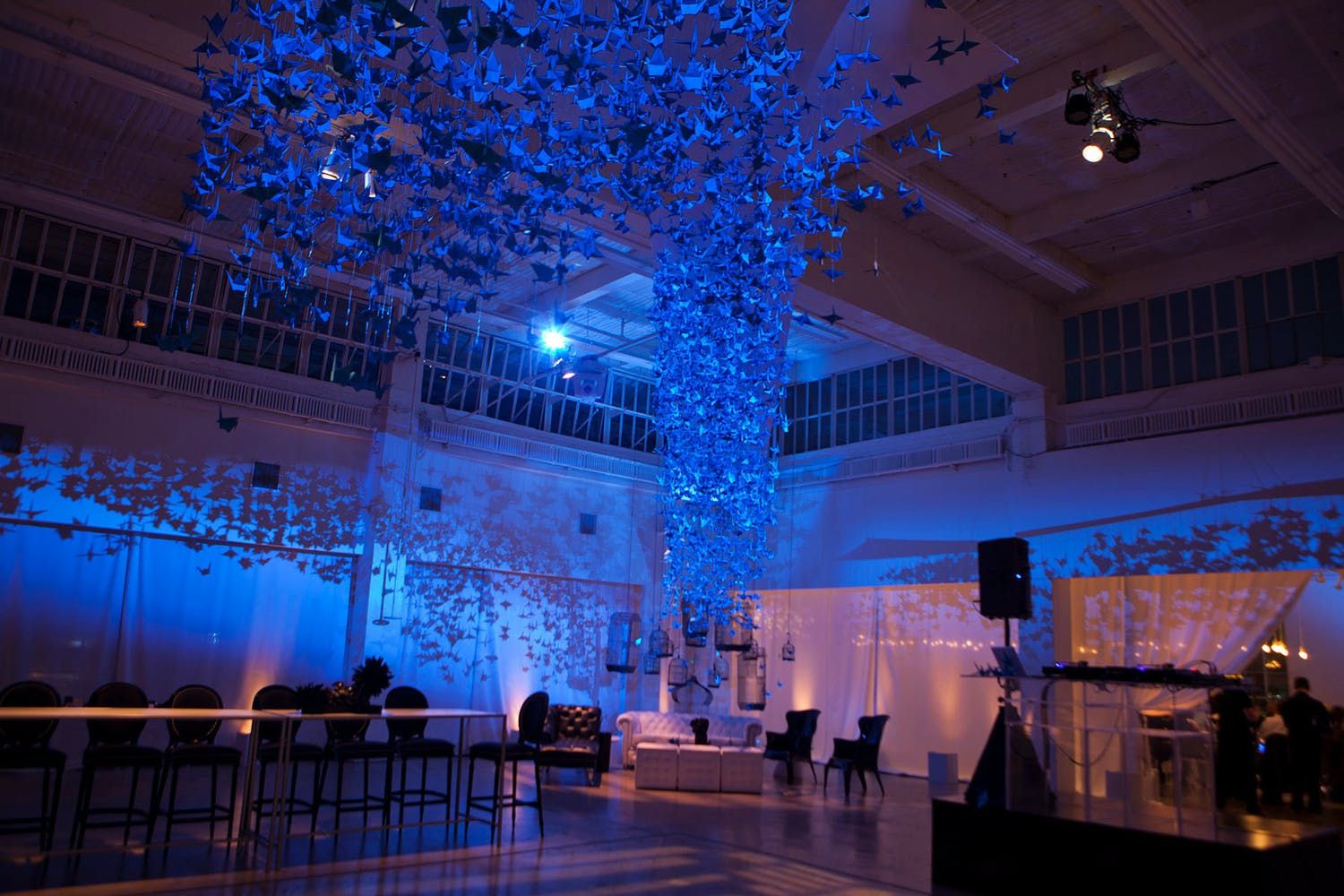 Ceiling installation of bright blue cranes against blue uplighting at wedding | PartySlate