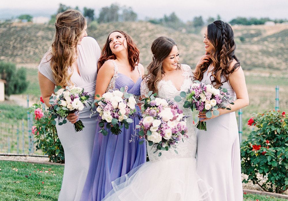 A bride posing with her three bridesmaids that are wearing periwinkle dresses.