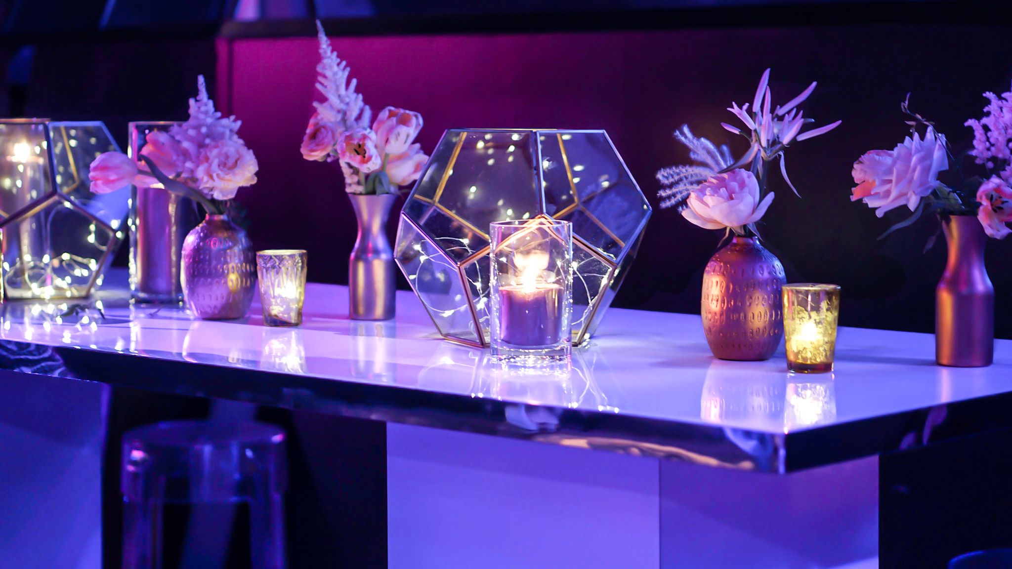 A table stand with candles lit and geometric vases filled with twinkle lights.