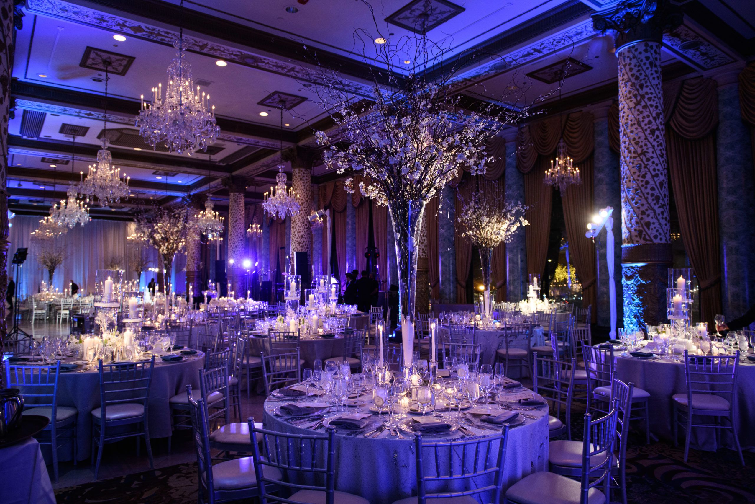 A peri-lit ballroom with round tables and lavish centerpieces