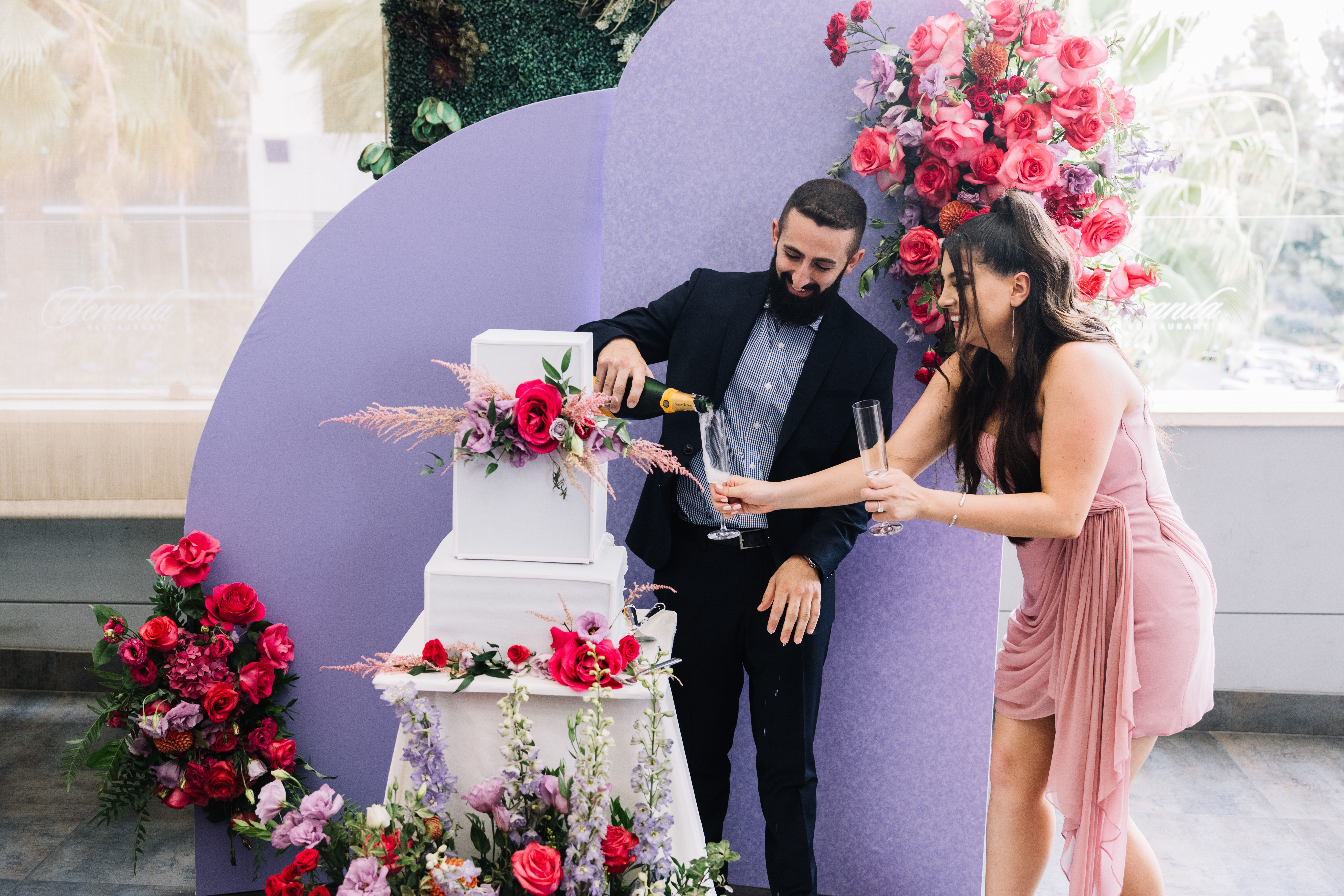 A bride and groom pouring a glass champagne beside their wedding cake