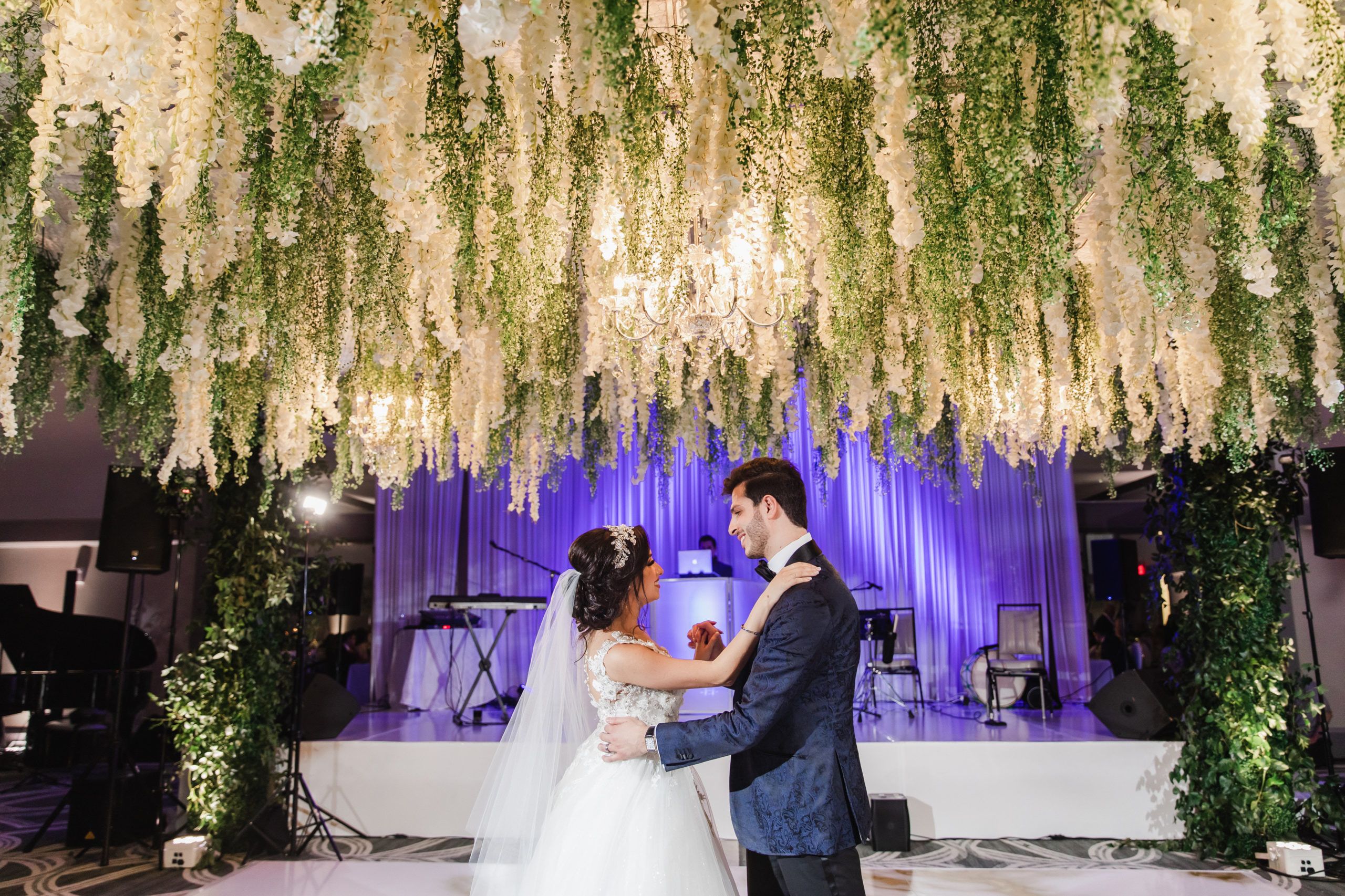 Wedding At The Omni Hotel In Houston Bride and Groom Dancing On Dance Floor Under Floral Ceiling Installation And DJ Booth | PartySlate