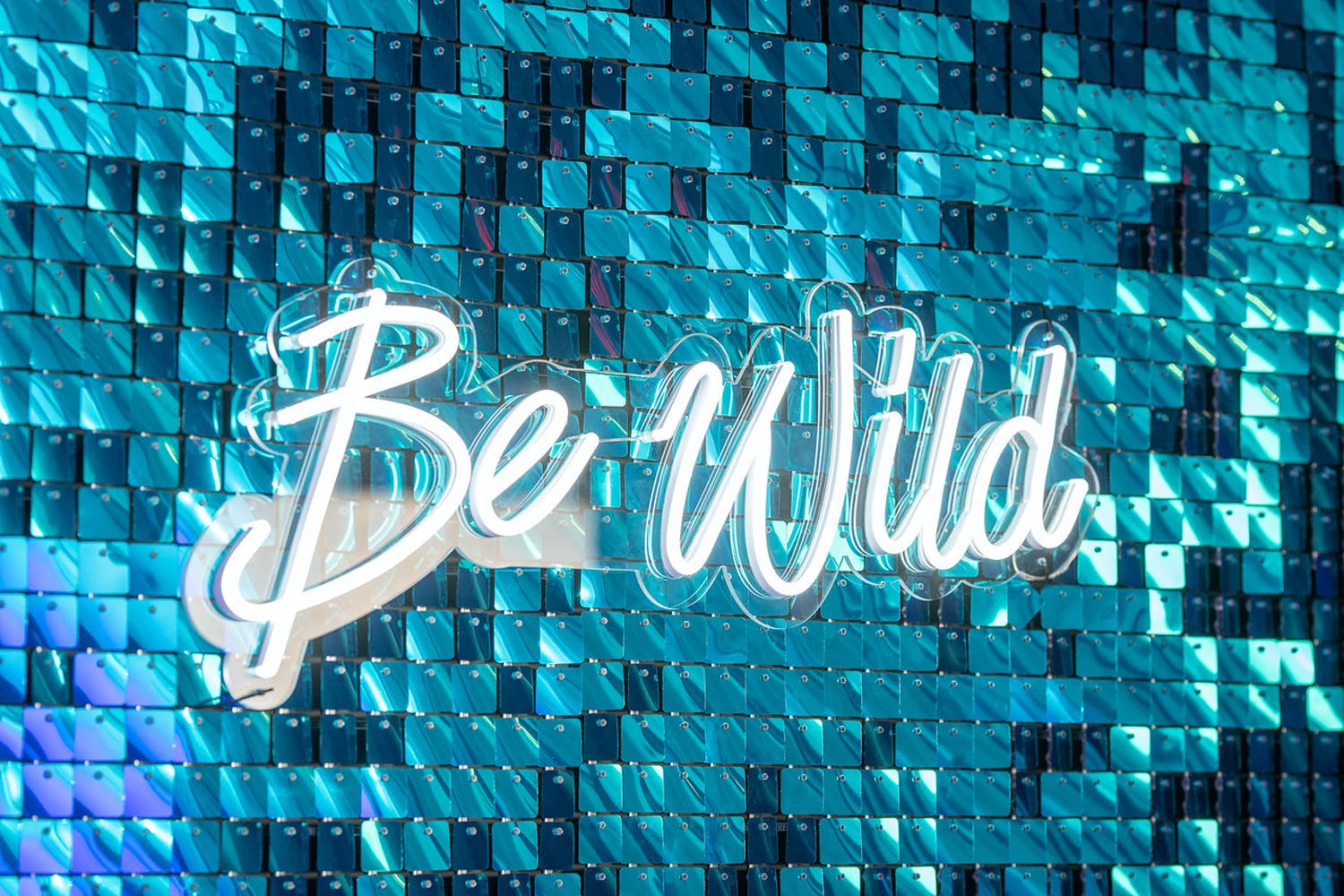 "Be Wild" white neon signage against checked blue glittery backdrop | PartySlate