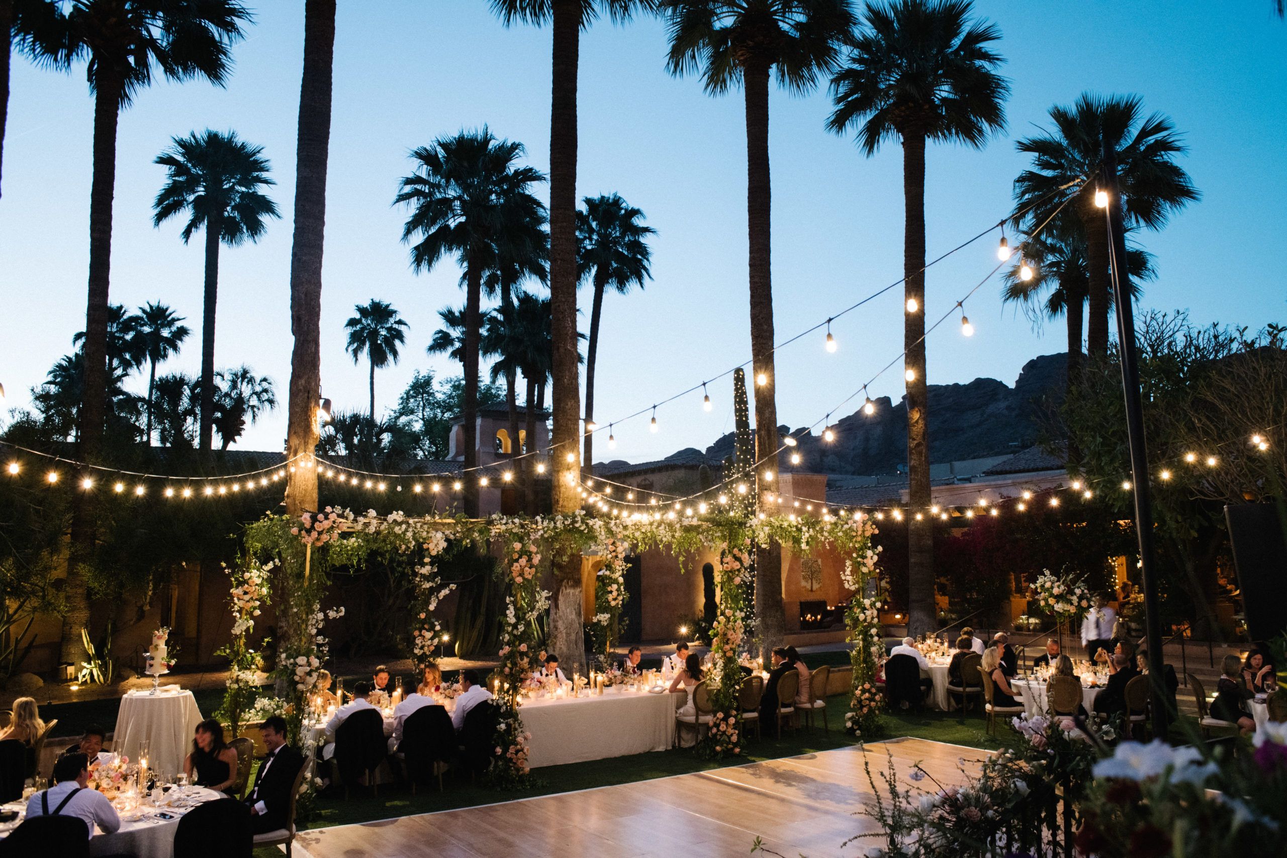 Outdoor wedding At Night With String Lights Hung Over Dance Floor and Tables With Guests Eating | PartySlate