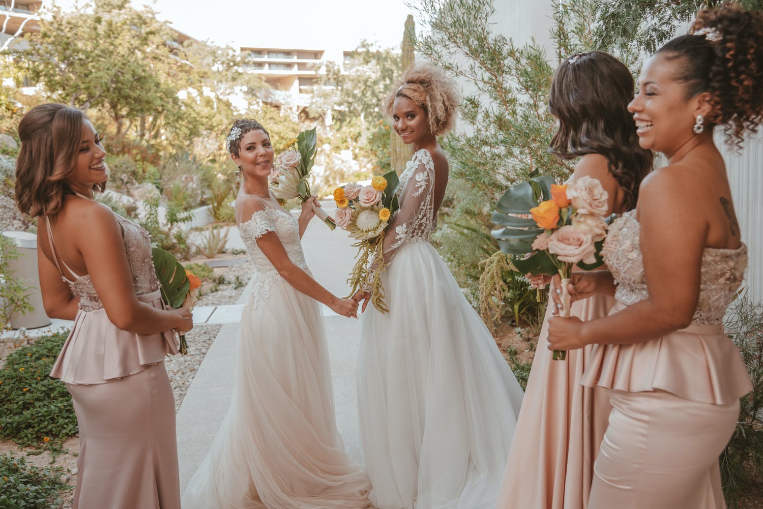 Brides and bridesmaids hold peach and gold flowers at desert beach wedding | PartySlate